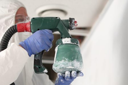 Close-up of professional foreman holding spray gun and painting wall in light colour. New apartment project renovation and interior design. Construction site and modern device concept